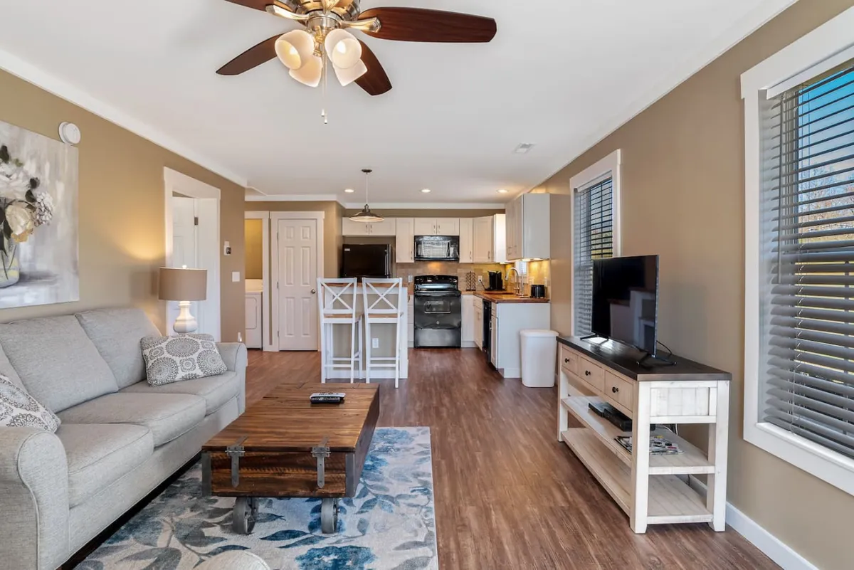 A cozy living area with a comfortable sofa, coffee table, television, and visible kitchen zone. The space is designed for relaxation and socializing, with warm lighting and an inviting layout that encourages effortless living.
